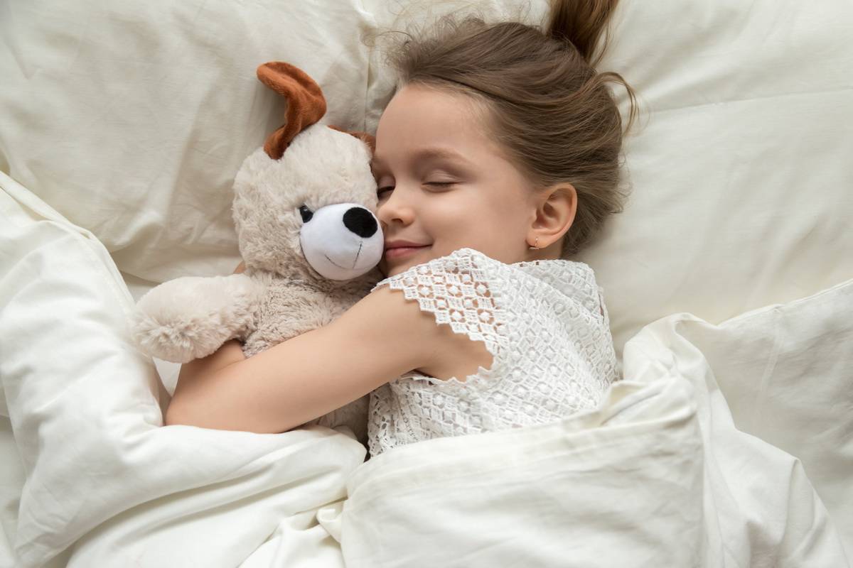 Fillette faisant un calin à son ours en peluche en dormant